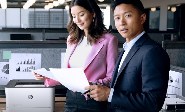 A woman and a man checking some prints while standing asid an HP printer.