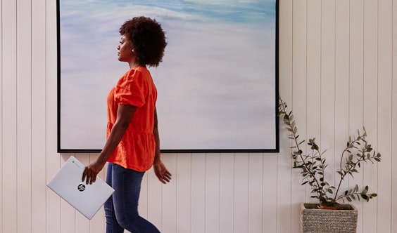 A woman walking on a living room while carrying an HP laptop in her hand.