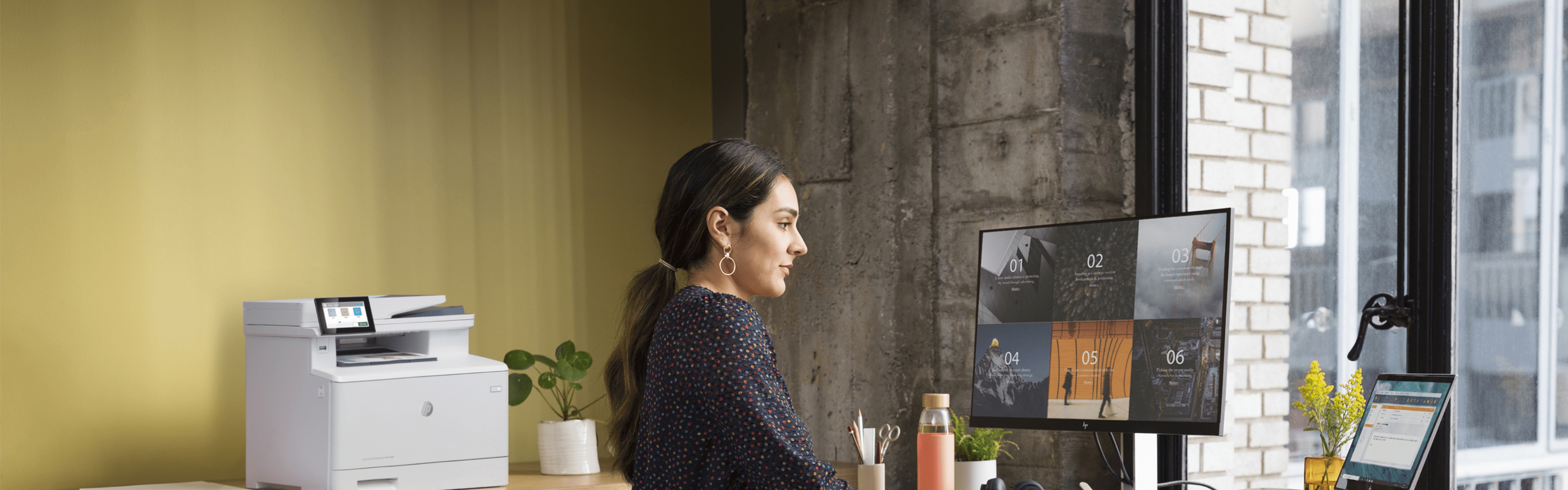 Woman at standup workstation looking at HP monitor next to HP LaserJet Pro printer