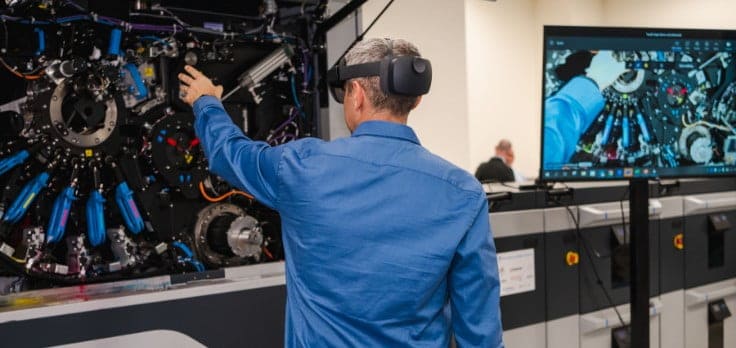 Man wearing HoloLens VR glasses, reaching out to HP Indigo digital press