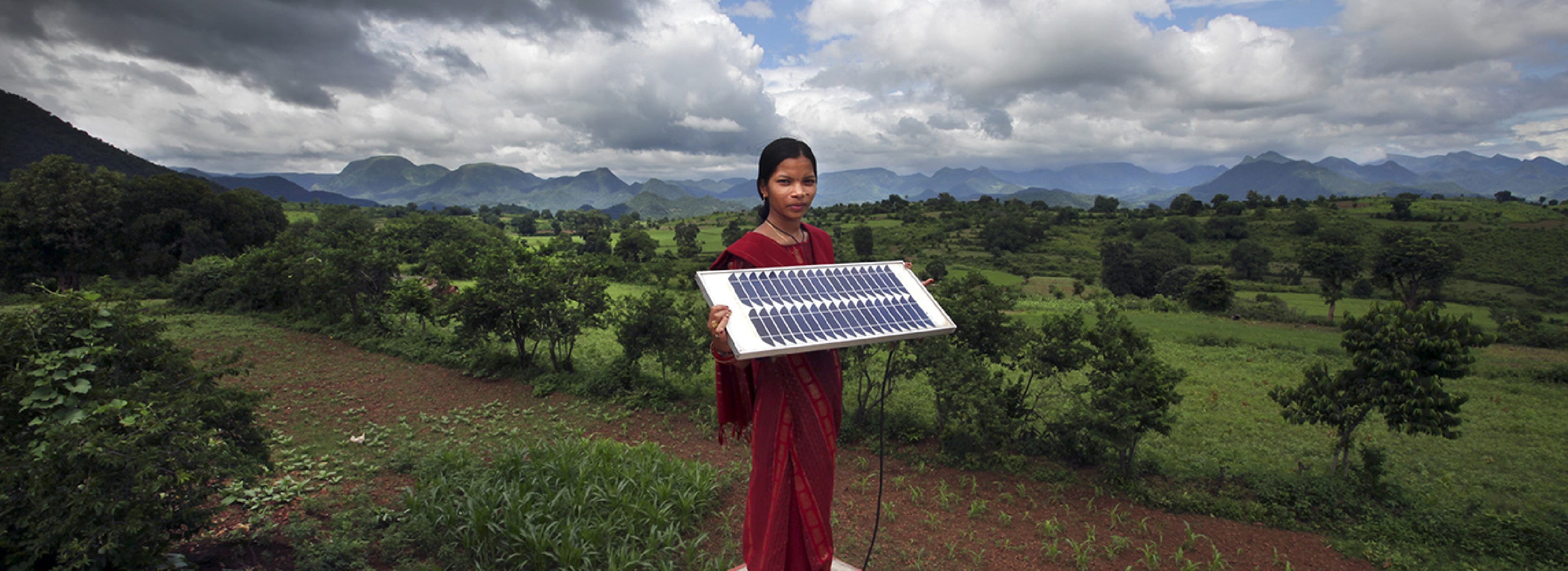 A girl holding a solar panel in a rural environment.