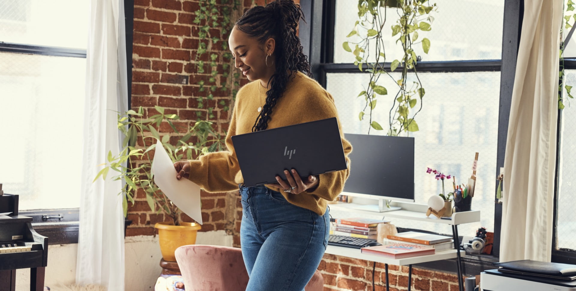 A woman working on her home office standing while carrying an HP laptop.