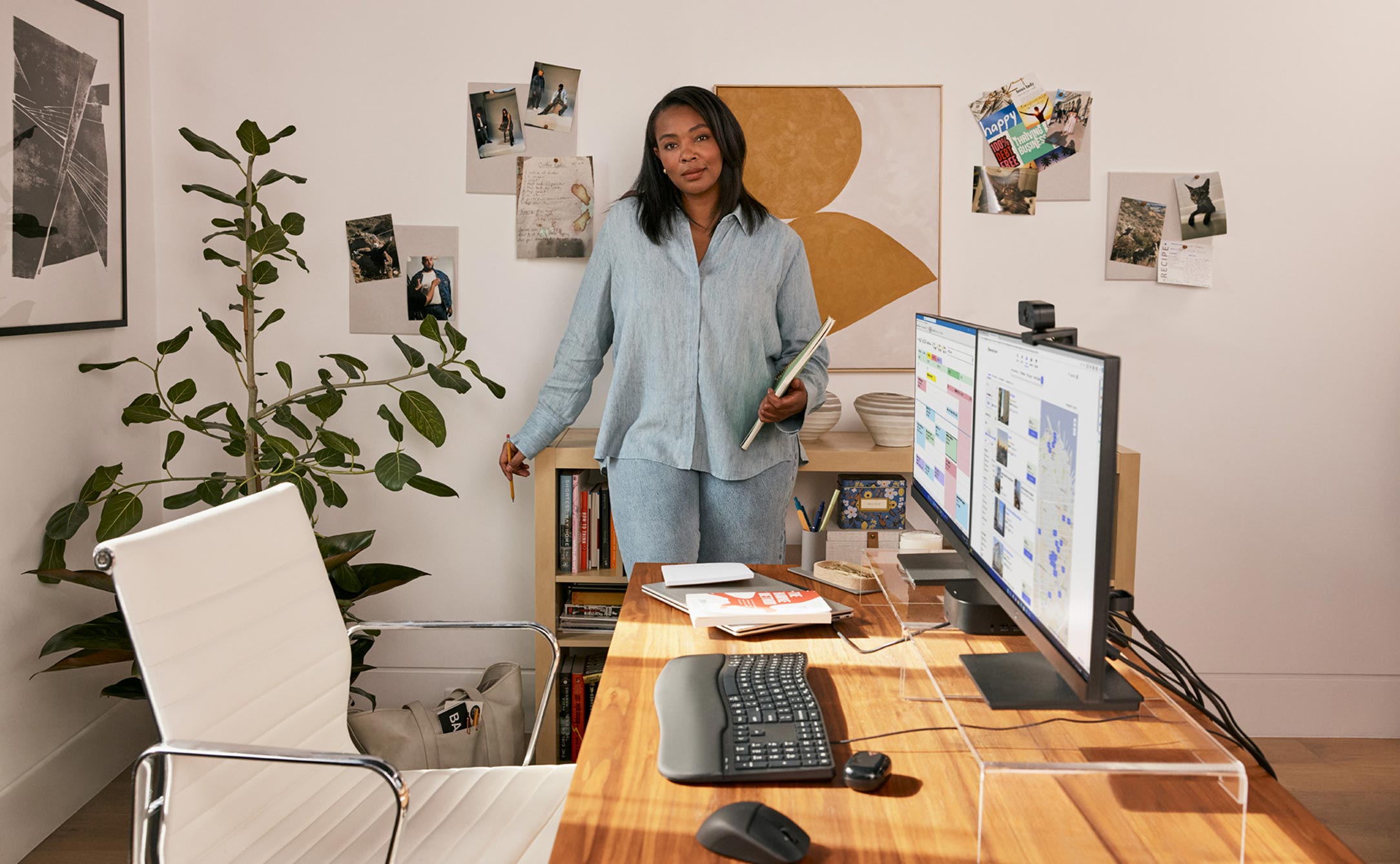 Woman working from home holding a notebook aside two HP monitors connected to an HP desktop mini.