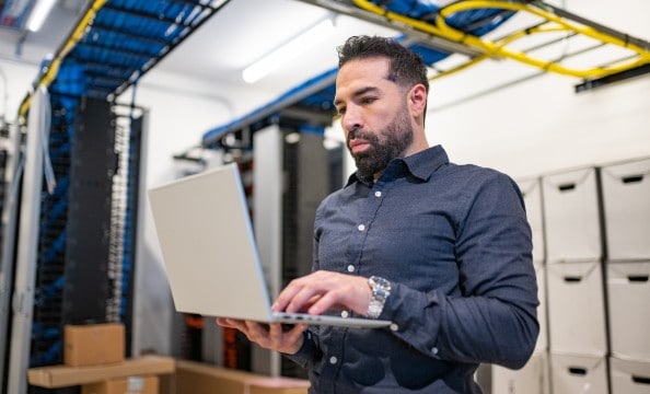 A man holding an HP laptop and typing while standing.