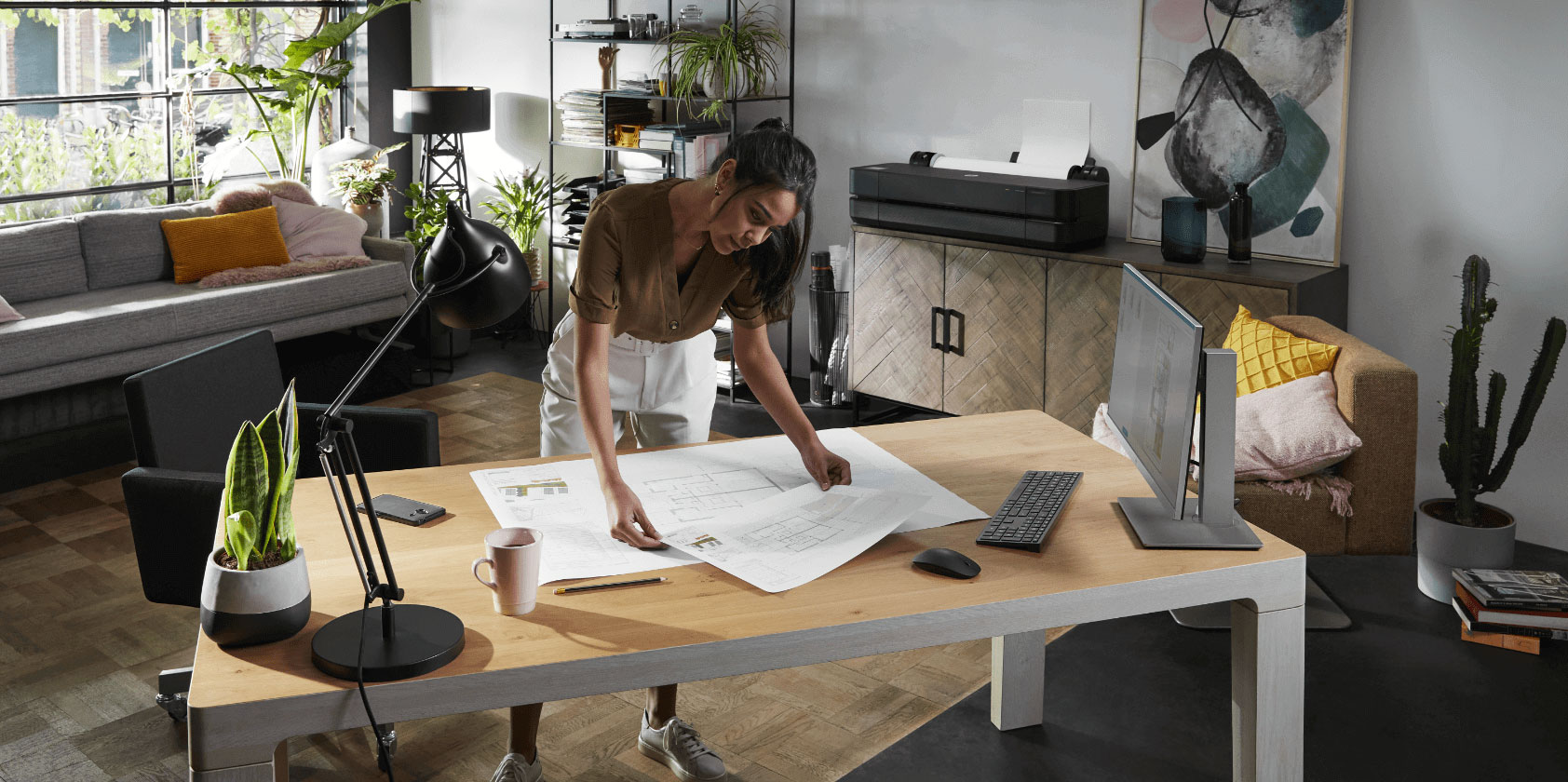 Person checking blueprints on a desk in an office next to an HP DesignJet plotter