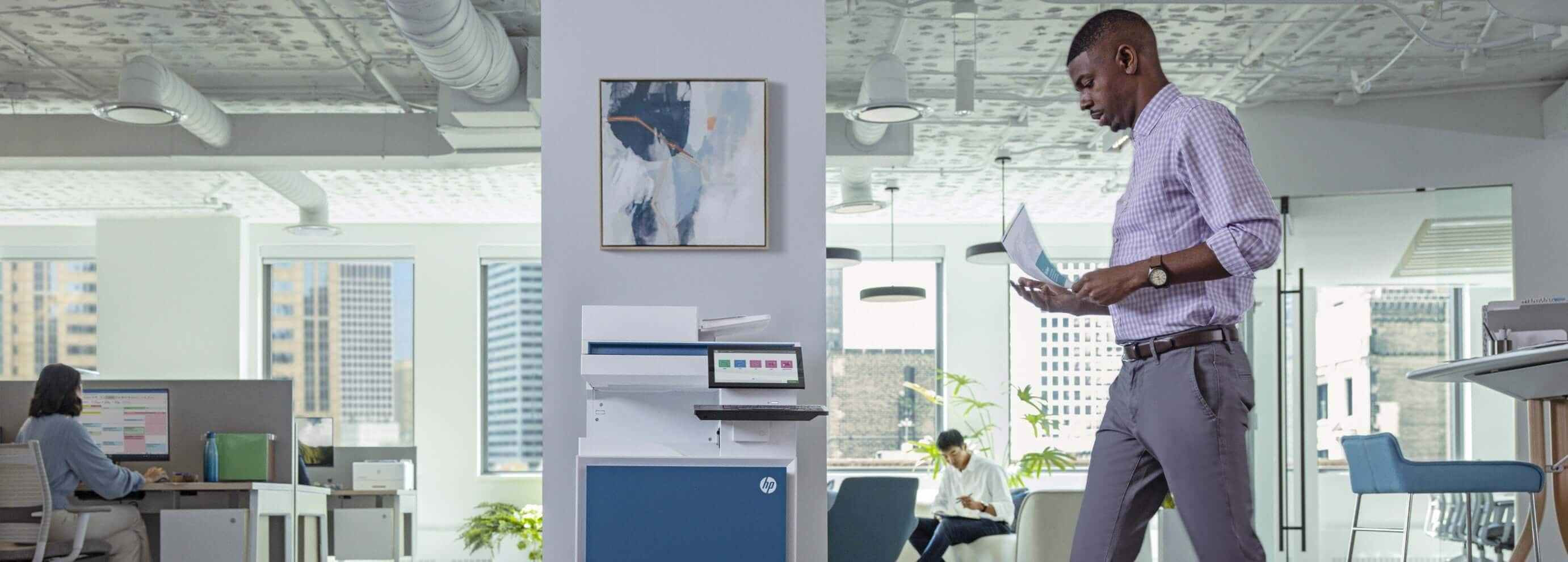 Male office worker looking at documents while standing at HP LaserJet printer