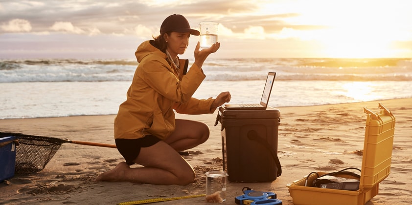 A woman looking at a water sample and taking some notes on her HP laptop.