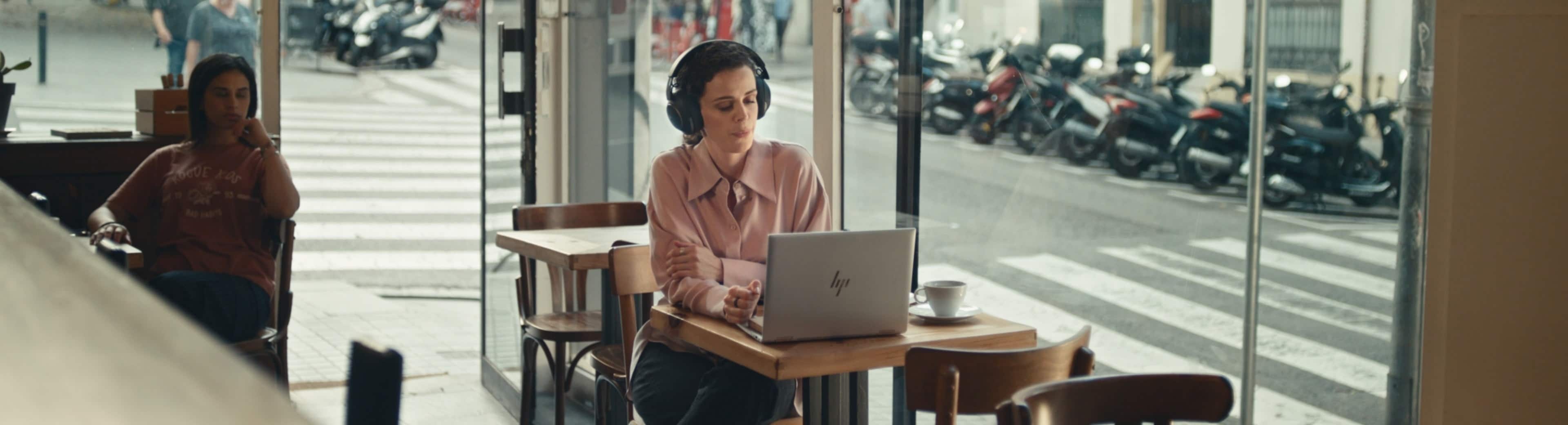 A woman wearing glasses and a blue sweater holding a Spectre x360 laptop in an office decorated with colorful paintings.