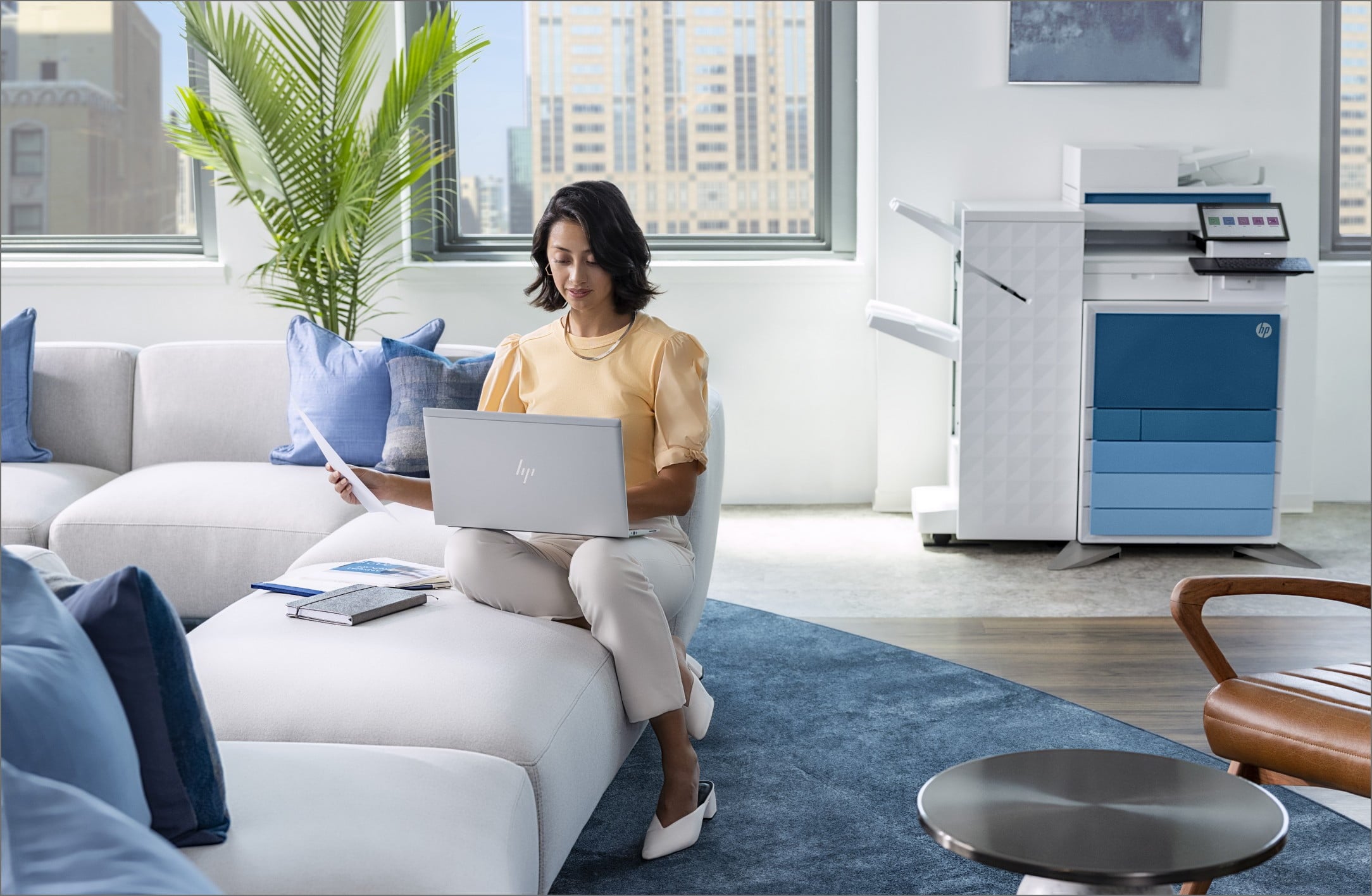 Woman in office lobby looking at HP EliteBook with HP LaserJet Managed printer behind her