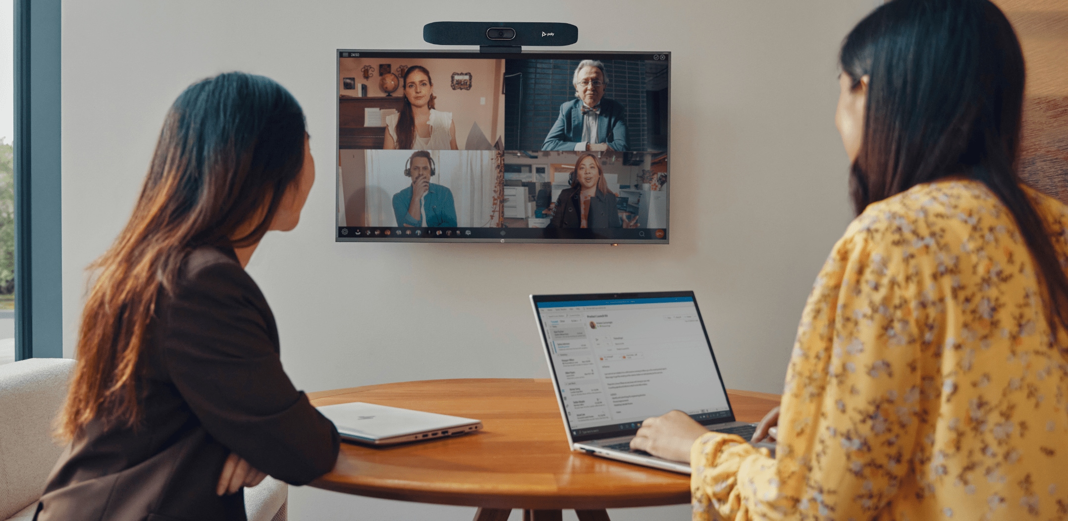 Two people in small meeting room using Poly Studio USB video bar during video conference 