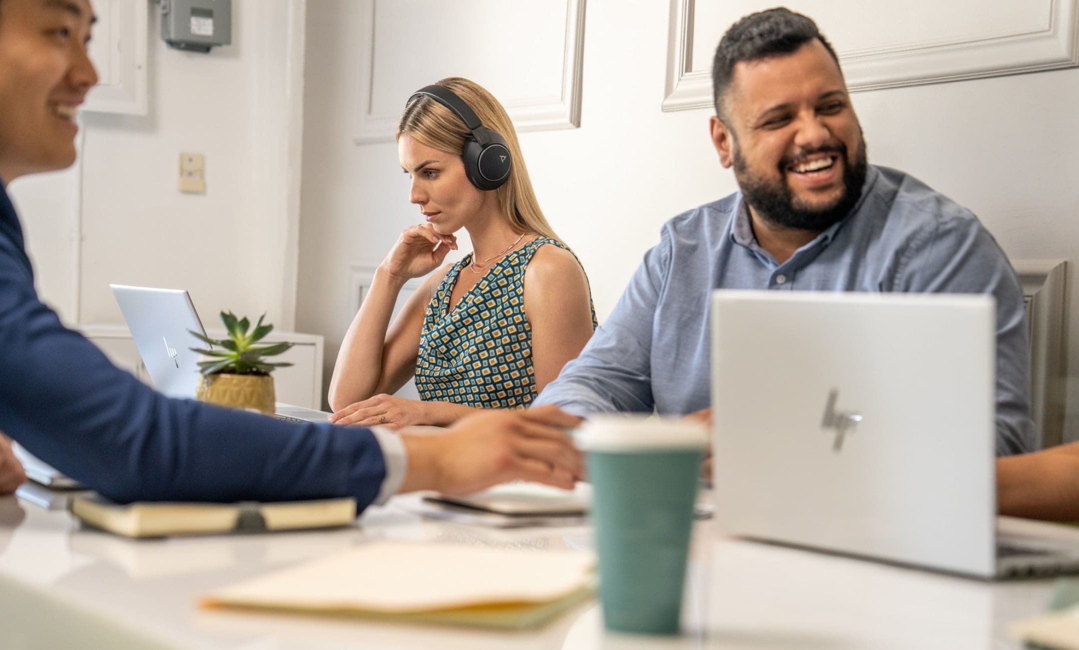 Woman in office wearing Poly Voyager Surround 80 bluetooth headset while seated at shared table