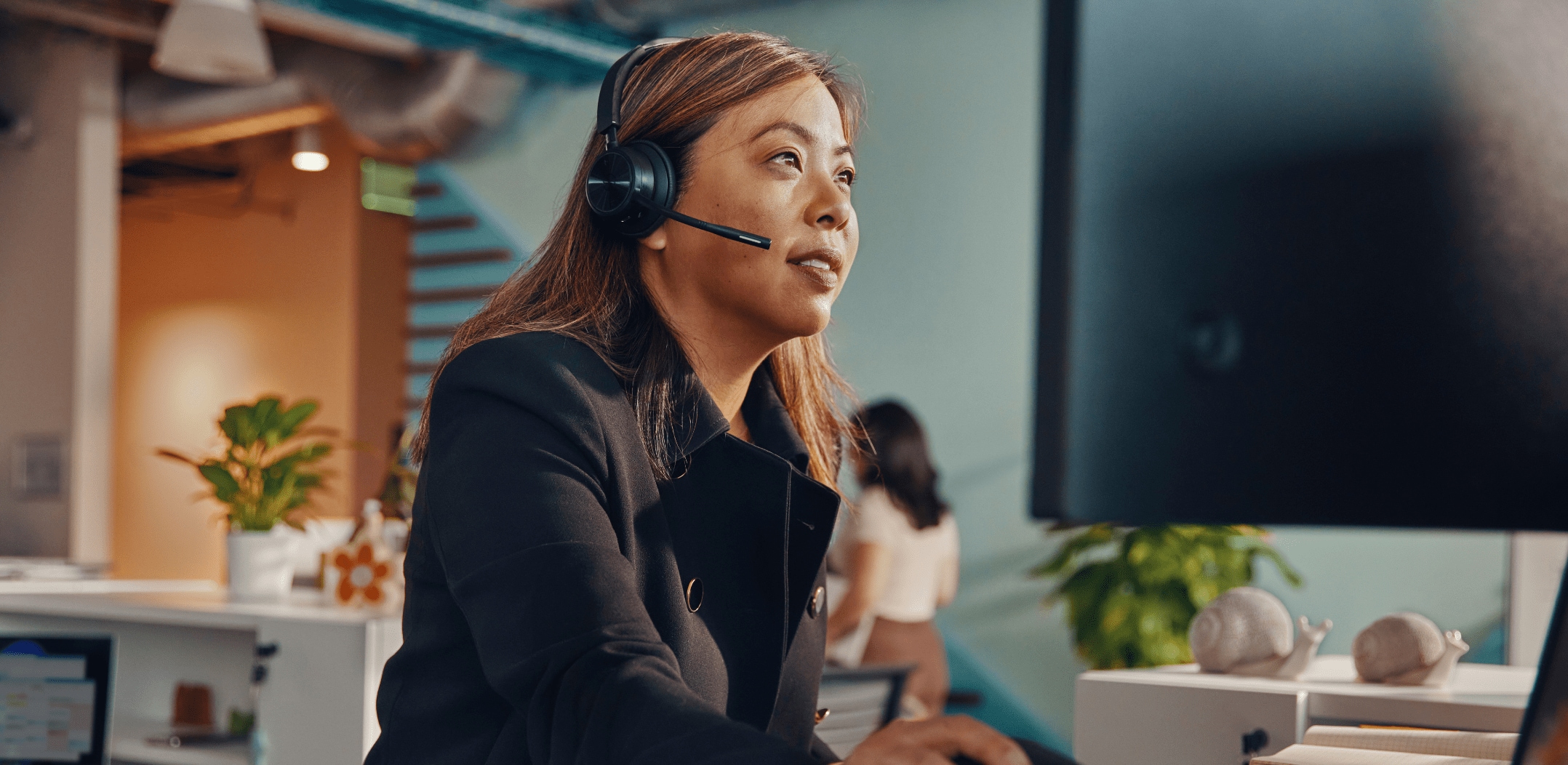 Woman at desk in open office wearing Poly Savi 7300 UC wireless DECT headset