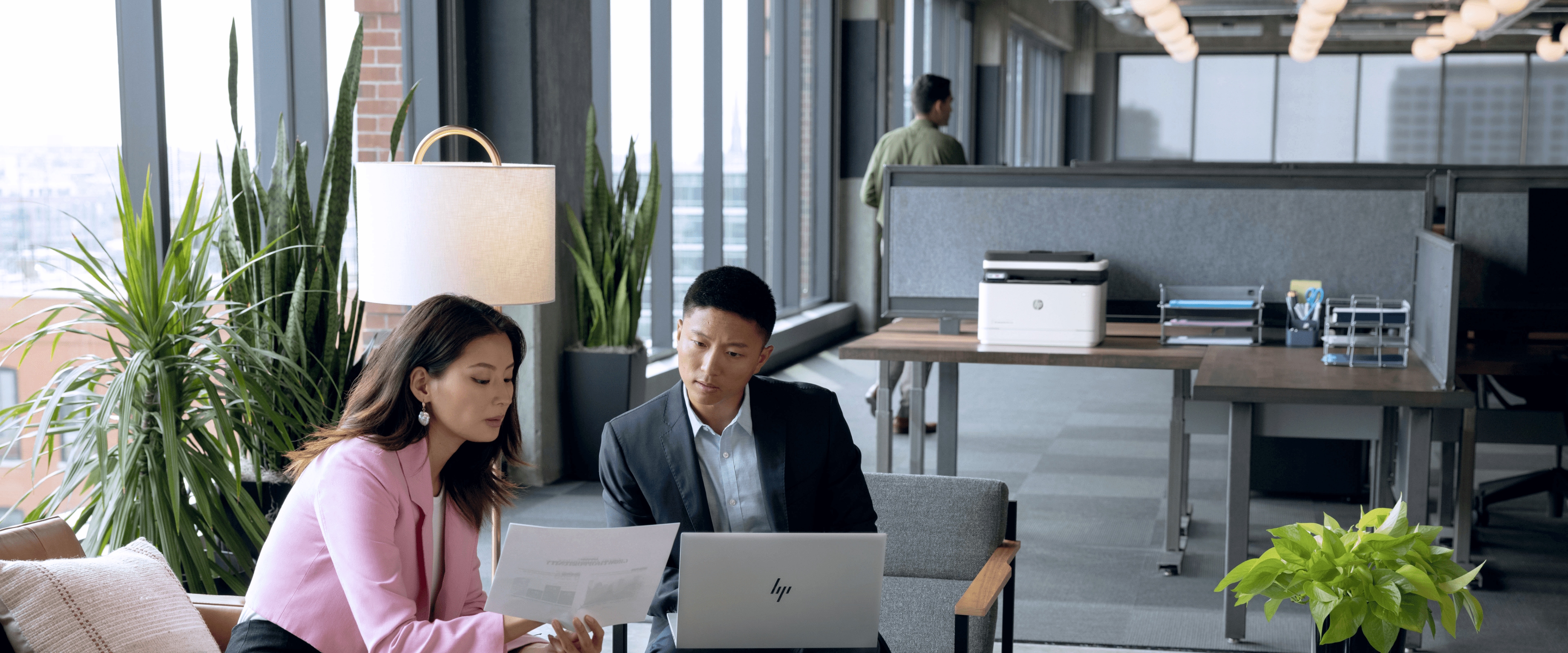 Man and woman in modern office looking at printed documents with HP LaserJet Pro printer  behind them