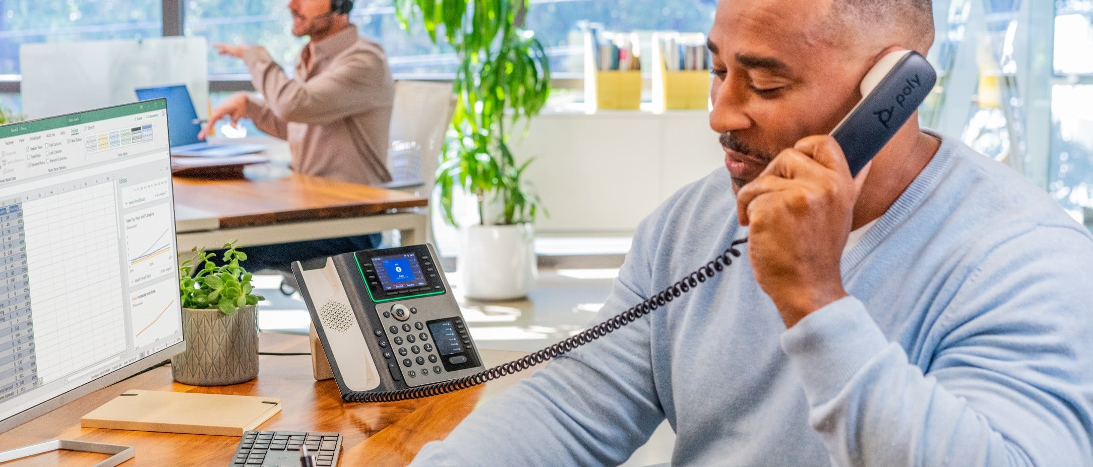 Man using Poly Edge E450 office IP phone with handset to his ear during call