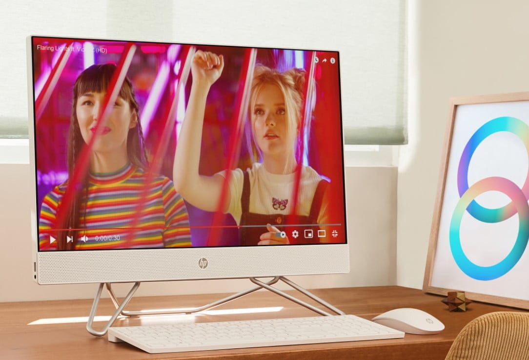 An HP All-in-One PC on top of a wooden desk aside some HP wireless keyboard and HP wireless mouse.