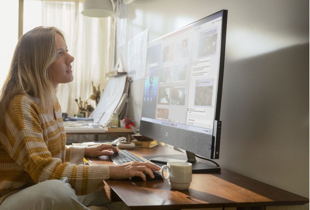 A woman working on her HP Pavilion All-in-One desktop on her desk aside a cup of coffee.