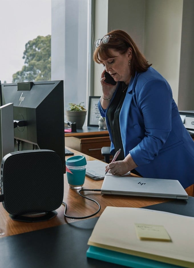 A woman taking some notes aside an HP laptop and an HP t640 Thin Client pc.