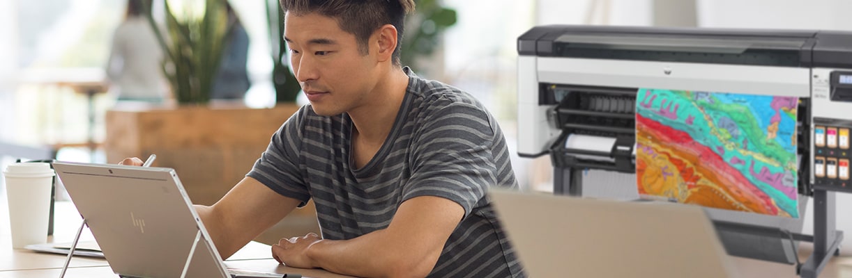 Person working in an HP device on a desktop next to an HP large-format printer