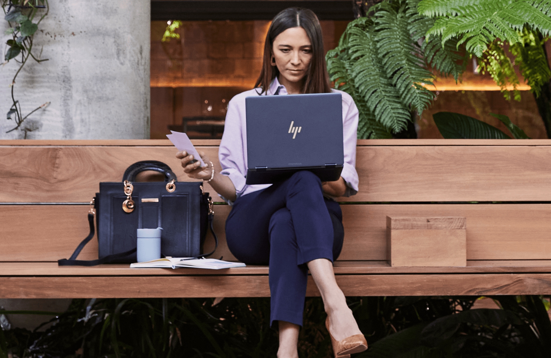 A woman sitting on a wooden bench while checking some data on her HP laptop on top of her lap.