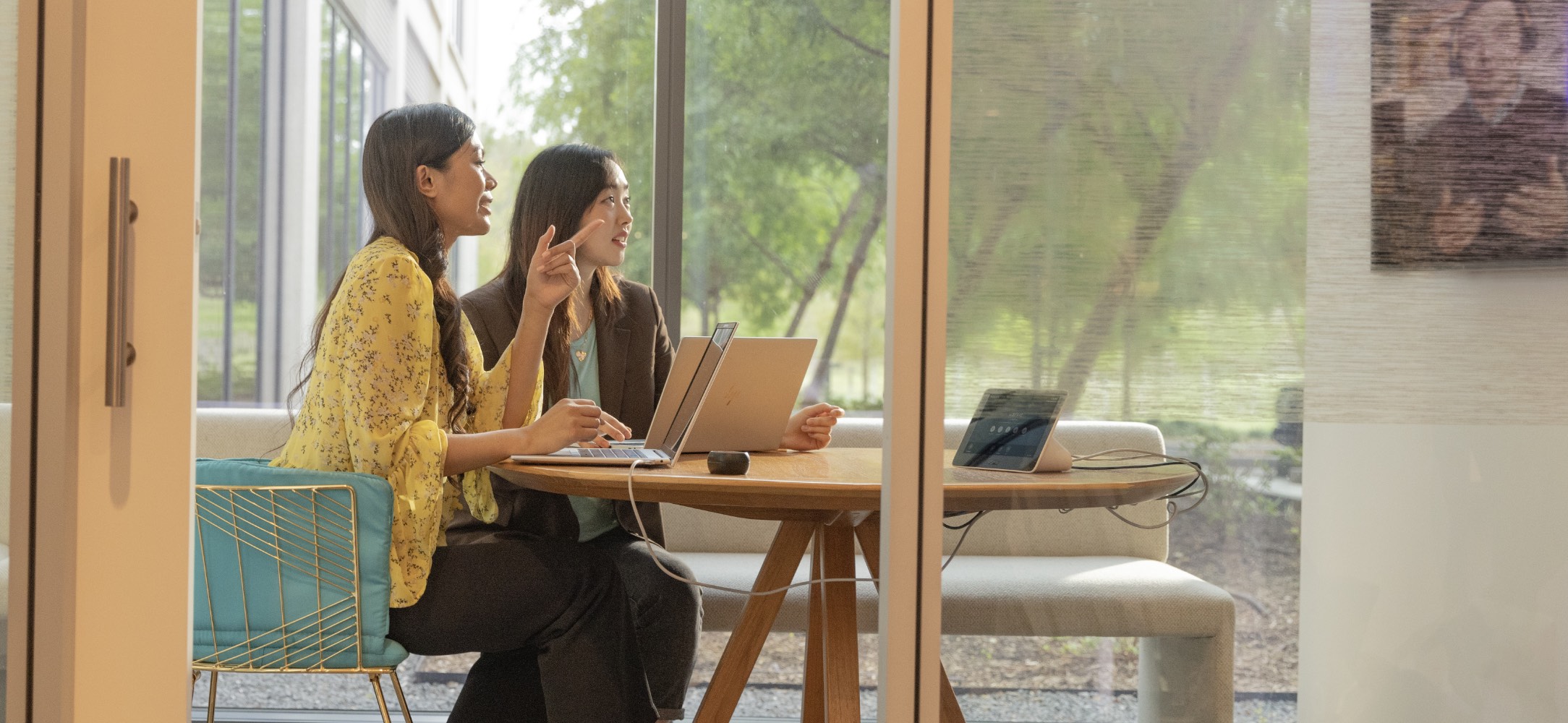 Two women in a conference room with HP Laptops over a desk