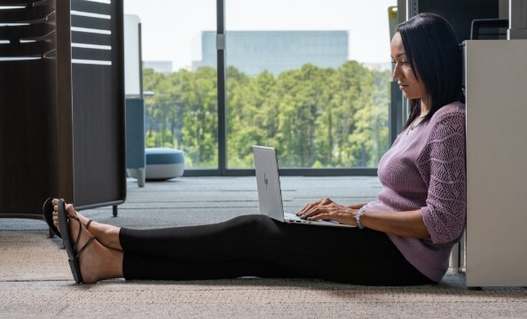 A woman sitting on the floor working on an HP laptop on her lap.