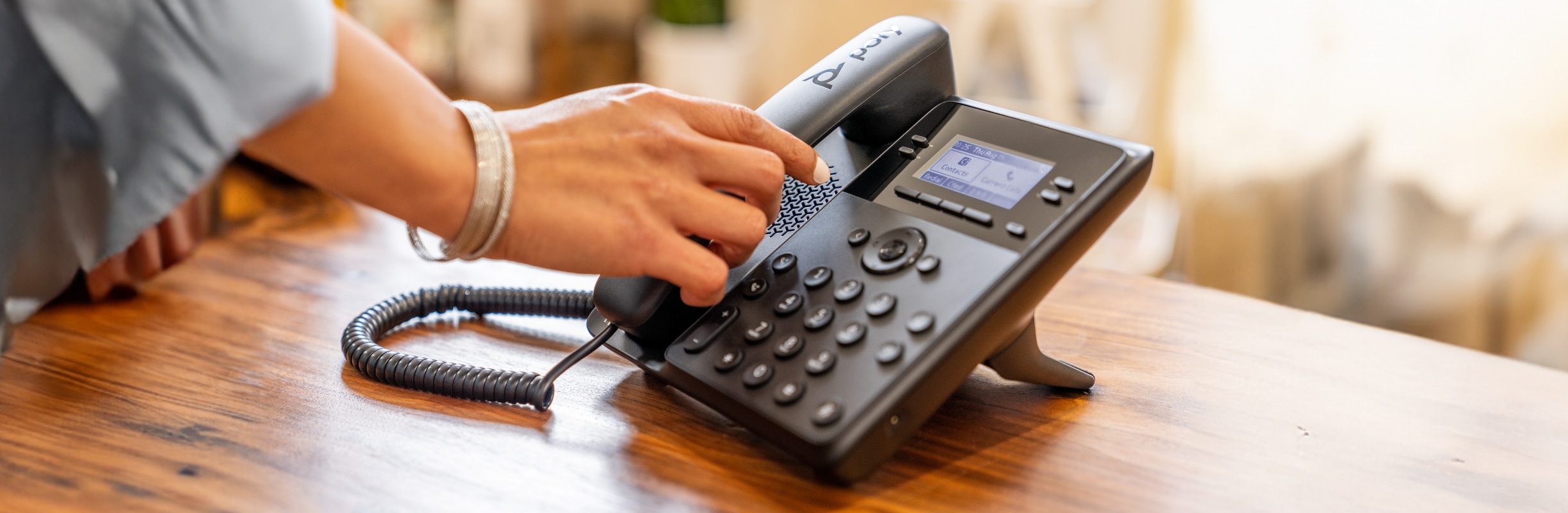 Woman's hand picking up the handset of a Poly Edge B30 IP desk phone on a wooden desk