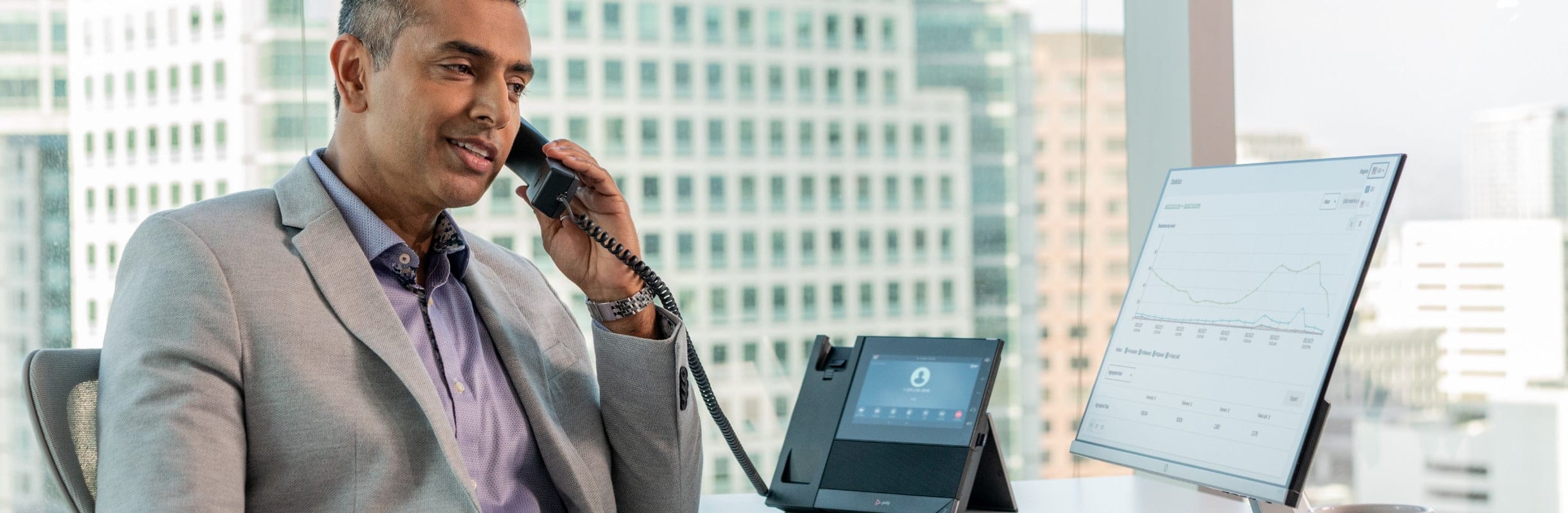 Man seated at office desk using Poly CCX 600 desk phone with handset during a call​