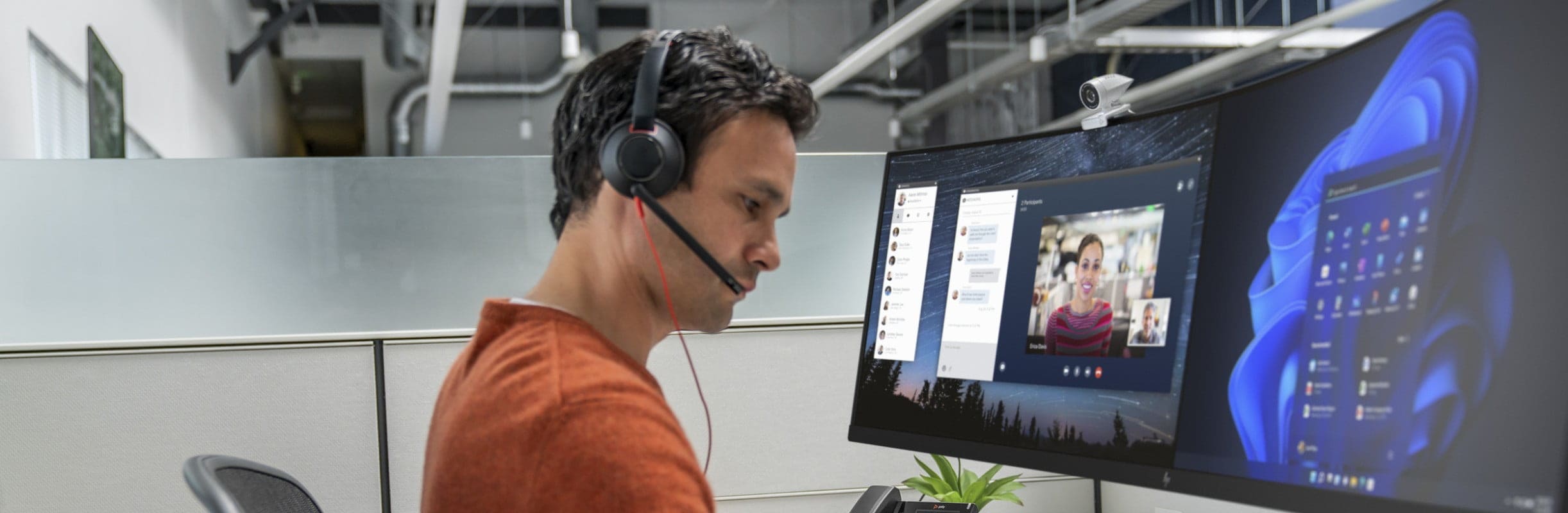 Man at desk in office cubicle, using Poly Blackwire 5200 USB wired headset connected to his desk phone during a video call