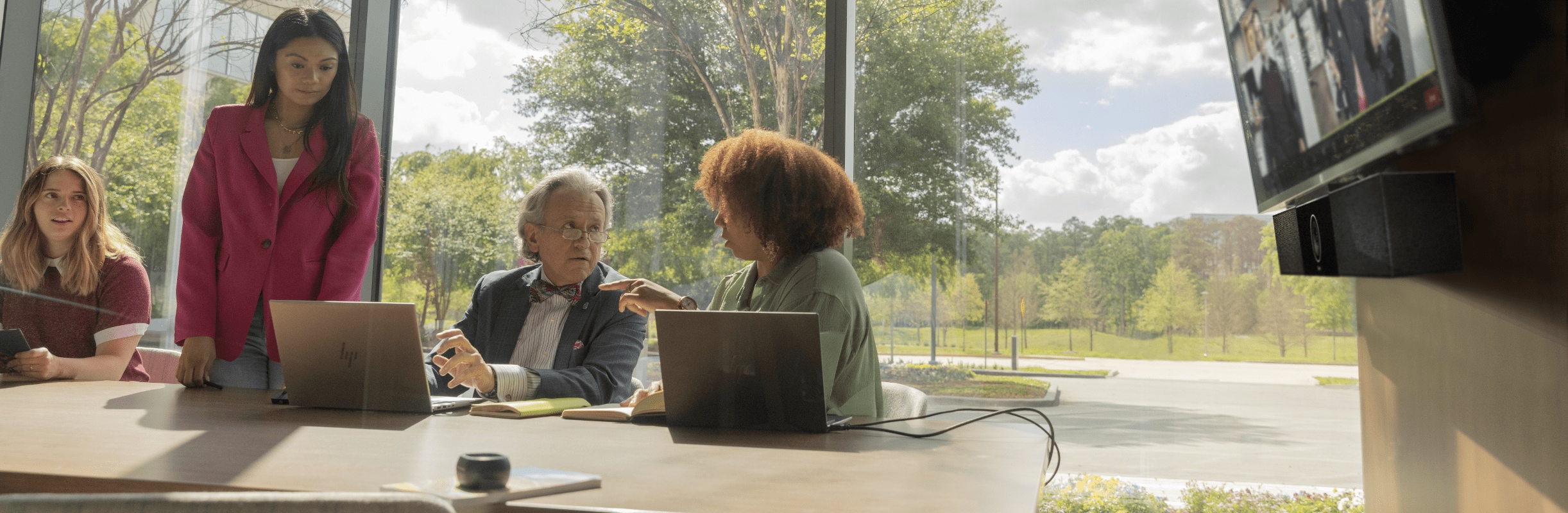 Small group of people in a medium galss-walled conference room during a video conferencing call using Poly Studio USB video bar 