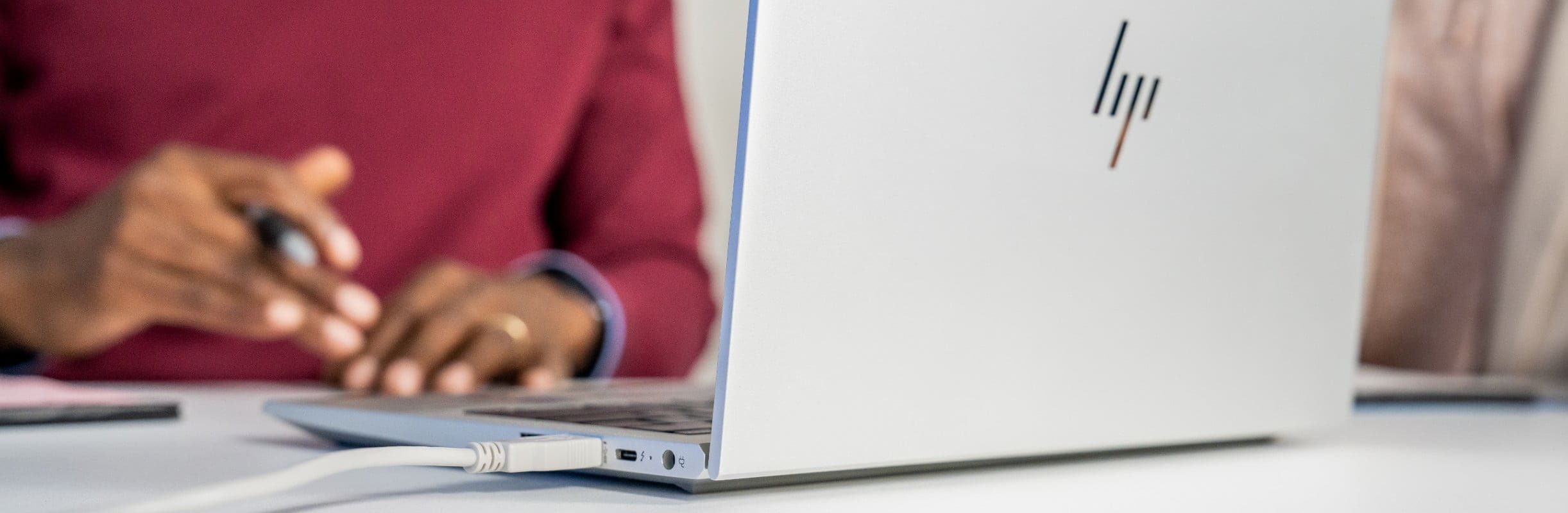 People seated around table using an HP laptop with USB cable attached to it from Poly USB video bar