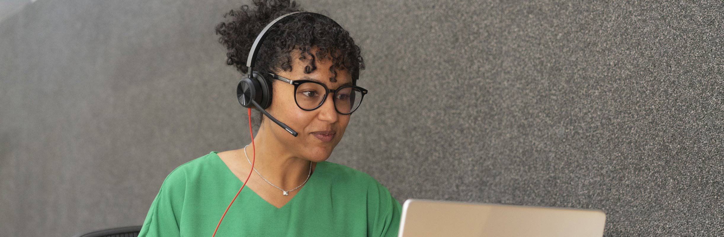 Woman working in office setting, wearing a Poly Blackwire 8225 USB wired headset and using the inline call controls