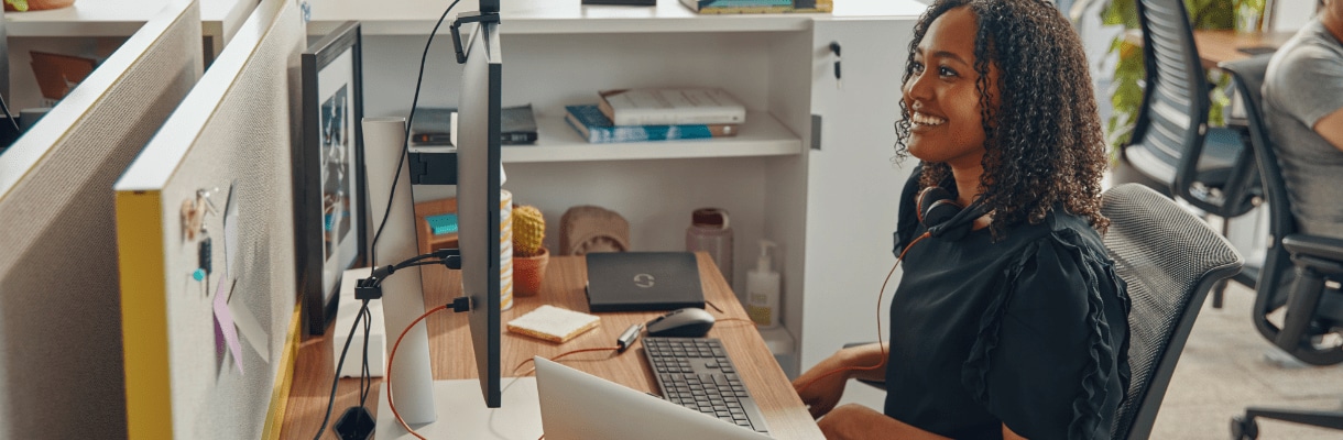 A woman looking at a screen of HP monitor with an HP webcam while using a Poly headset.