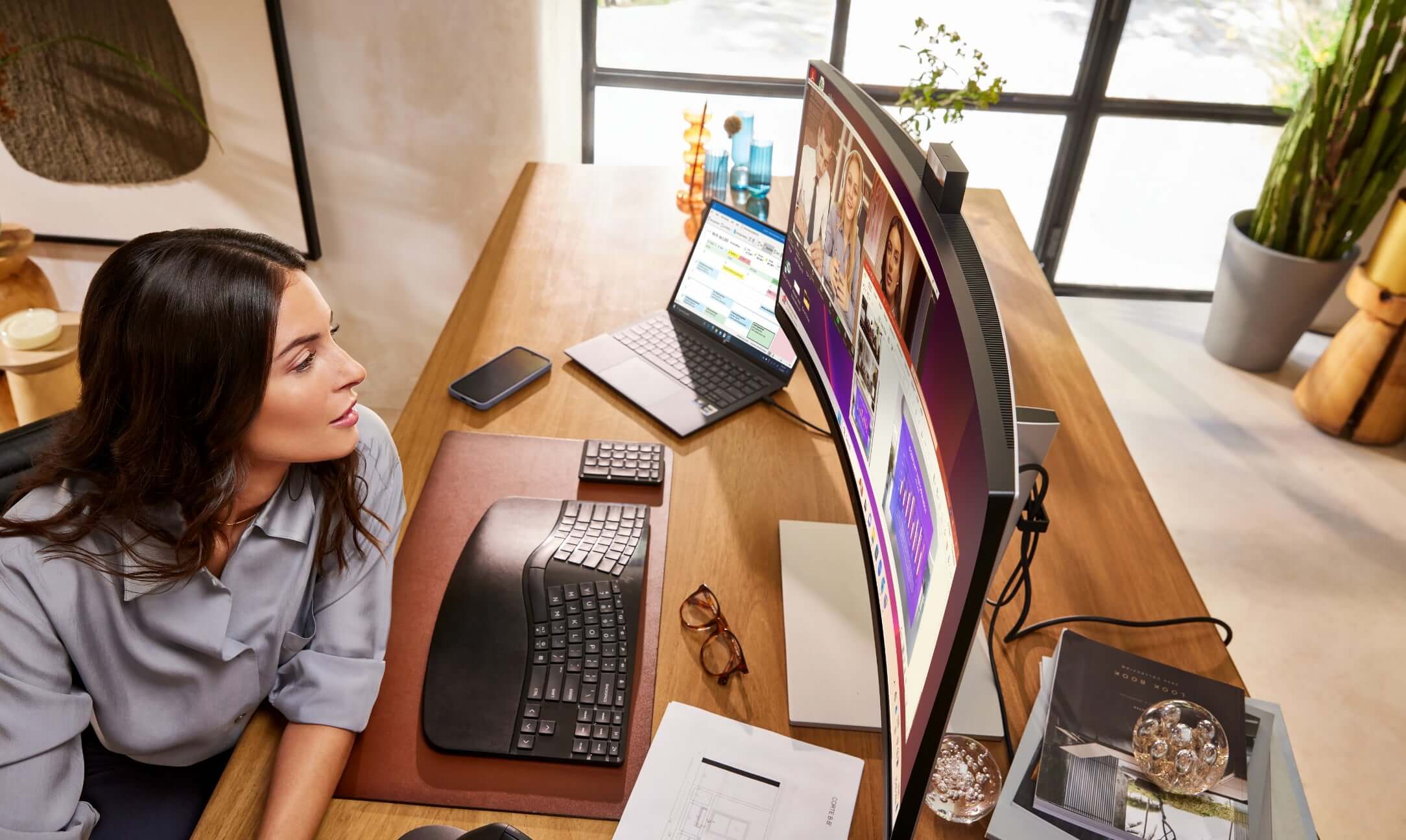 A woman having a virtual conference on an HP wide curved monitor connected to a Z HP laptop.