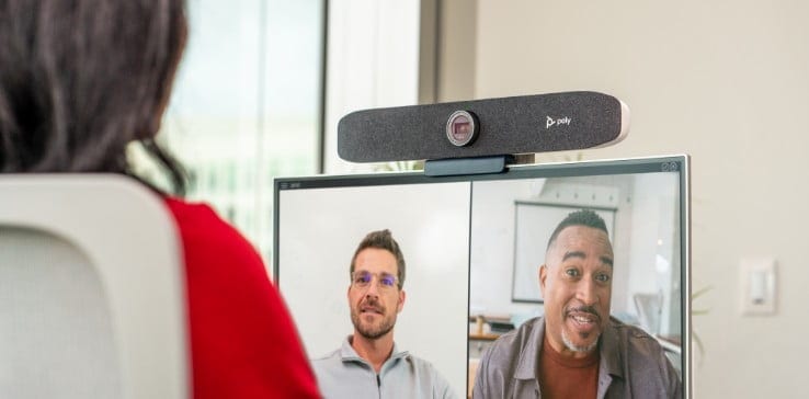 Looking over shoulder of person at office desk during video call using Poly Studio P15 video bar atop monitor