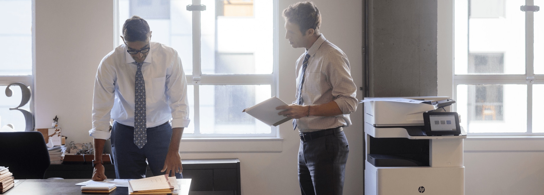 Two men in office talking about printed documents with HP LaserJet Enterprise printer next to them