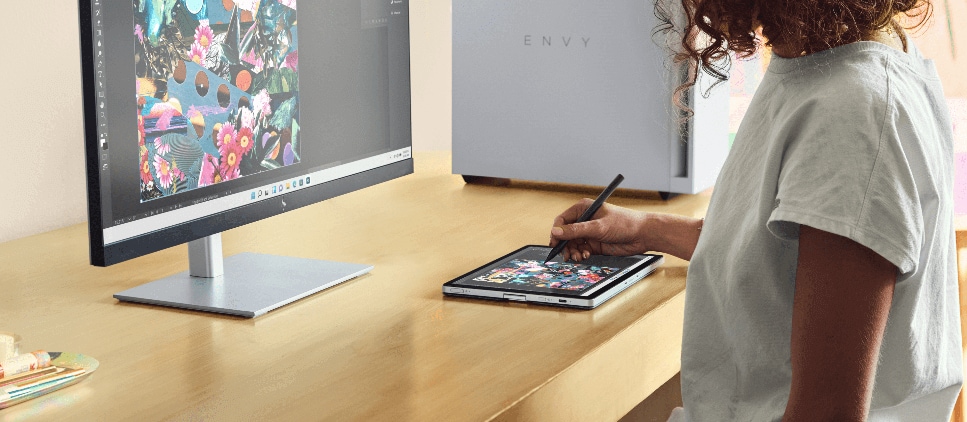 Woman drawing with a digital pen over a tablet that is connected to an HP Monitor and the HP Envy Desktop