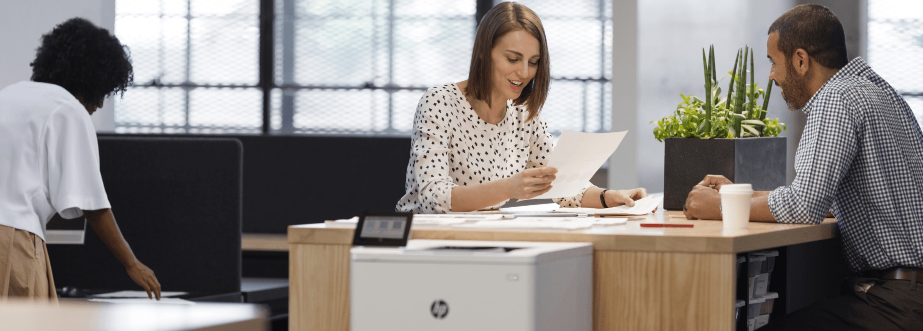 Smiling woman looking at printed document talking to man across desk with HP LaserJet Pro next to them