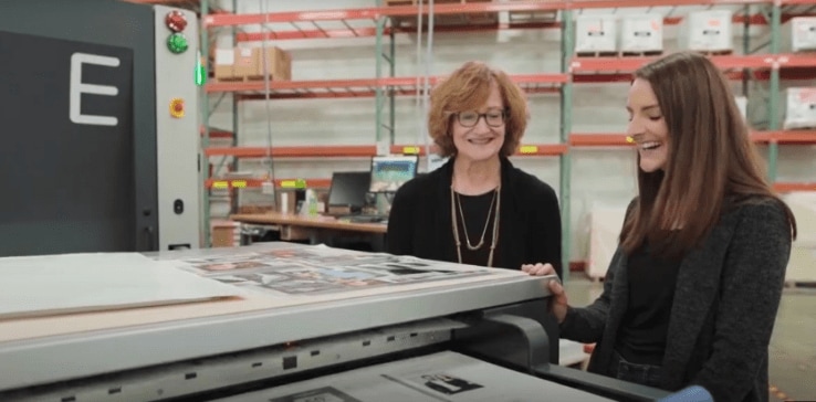 Two women leaning on a large printer