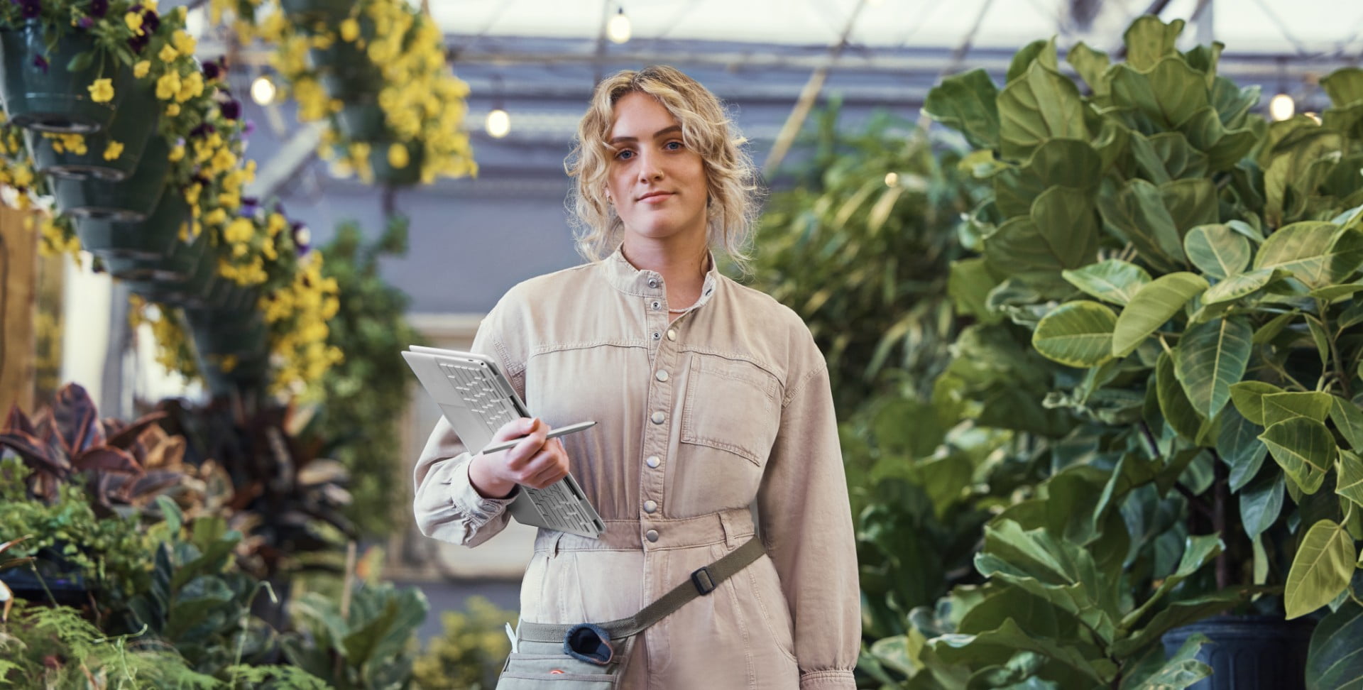 Woman standing in room full of plants holding HP Spectre x360 as a tablet with wireless pen in hand 