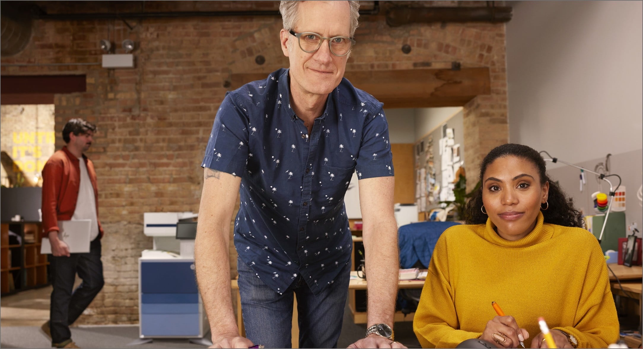 Standing man and seated woman in small office setting with HP LaserJet Managed printer behind them